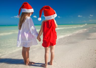 Little cute girls in Christmas hats on the exotic beach